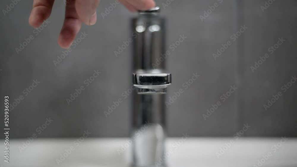 Water coming out of a chrome bathroom faucet at home being turned off. Detail frontal view with blurry background. Water coming out of a chrome bathroom faucet at home being turned off. Detail frontal view with blurry background.