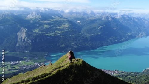 Aerial drone shot of a man standing on a cliff on a clear blue day with a view of the scenery of Lake Brienz, close to Brienzer Rothorn and the stunning European Alps of Switzerland photo
