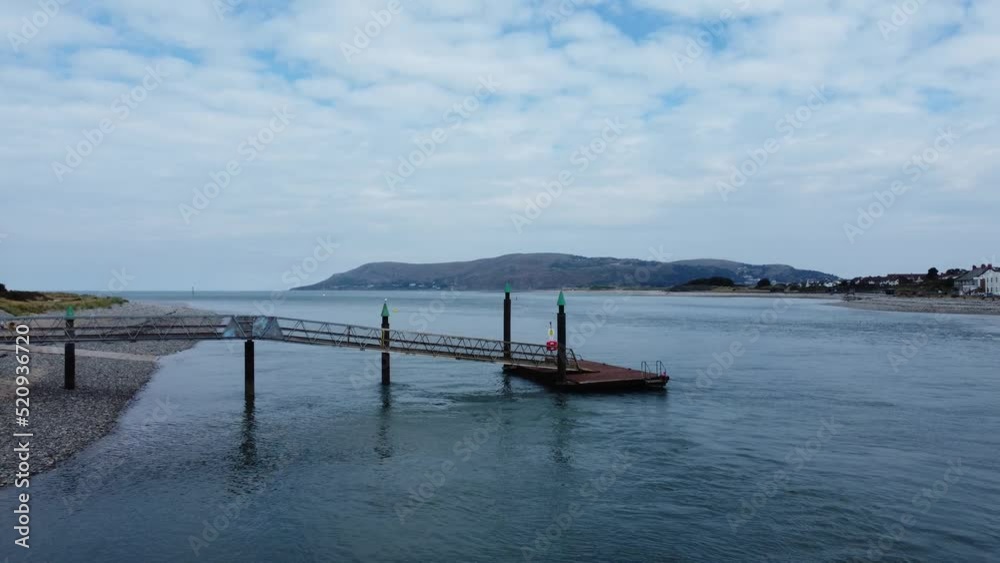 Metal jetty fishing platform aerial flyover view across North Wales coastline towards mountains