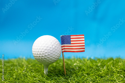 Golf ball with Flag of America on green grass with blue sky background 