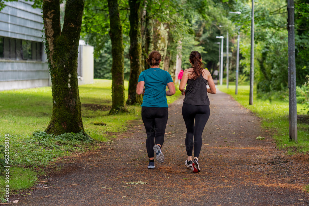 Fototapeta premium Two woman running on a footpath in park. Back to camera. Active and healthy lifestyle concept. Jogging to stay positive and increase endurance. Selective focus.