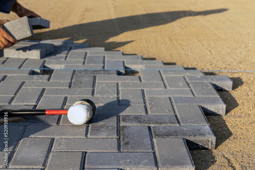 Hands of a worker installing concrete blocks, paving slabs with a rubber mallet. Selective focus.