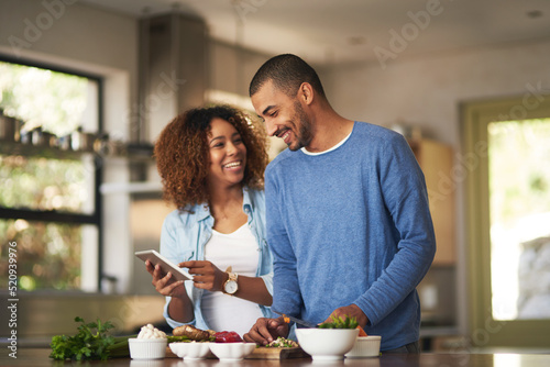 Our food looks just as good as the recipe. Shot of a happy young couple using a digital tablet while preparing a healthy meal together at home.