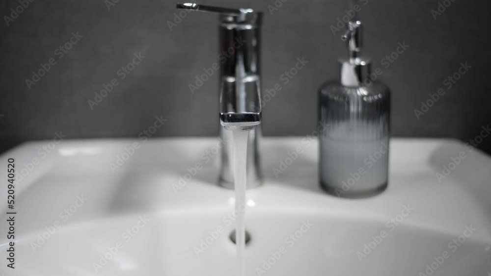 Chrome faucet in the bathroom of a designer loft being turned on by caucasian hand. Chrome faucet in the bathroom of a designer loft being turned on by caucasian hand.