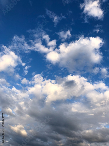 bright summer blue sky with white fluffy clouds of various shapes and sizes  cirrus  heap clouds  golden from sunlight.