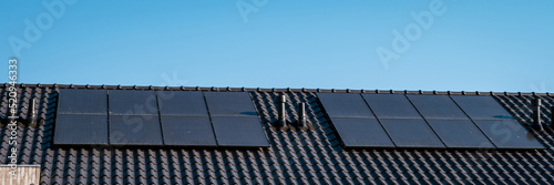 Newly build houses with solar panels attached on the roof against a sunny sky Close up of a new building with black solar panels. Zonnepanelen, Zonne energie, Translation: Solar panel, , Sun Energy.  photo