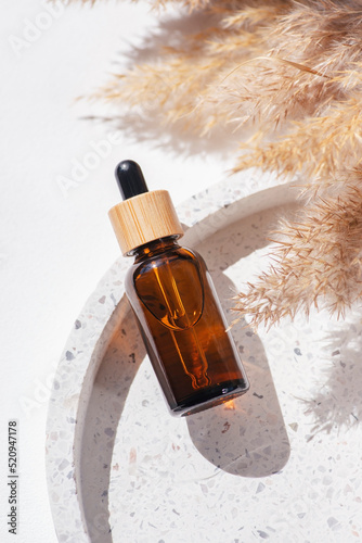 Amber glass dropper with bamboo lid and dry plant. Bottle on the terrazzo podium for product presentation. Skincare cosmetic with wildflowers. Beauty concept