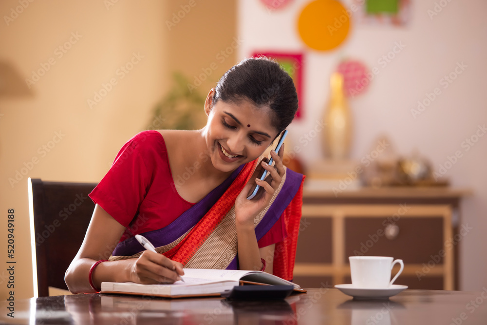 Smiling woman taking notes while talking on mobile phone Smiling woman taking notes while talking on mobile phone