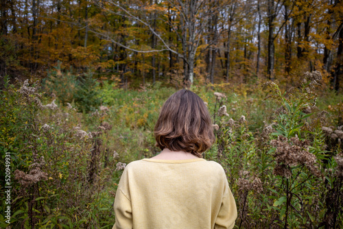 Short haired woman in yellow shirt walks through unkempt rustic woodland landscape in fall foliage  photo