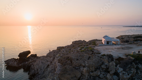 Aerial bird’s eye view of coastline sunset and landmark white washed chapel Agioi Anargyroi, Cavo Greco Protaras, Famagusta, Cyprus from above. The sea cliff rock Ayioi Anargiroi church at sunrise. photo