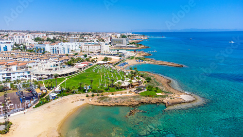 Aerial bird's eye view Pernera beach Protaras, Paralimni, Famagusta, Cyprus. The tourist attraction golden sand bay with sunbeds, water sports, hotels, restaurants, people swimming in sea from above. 