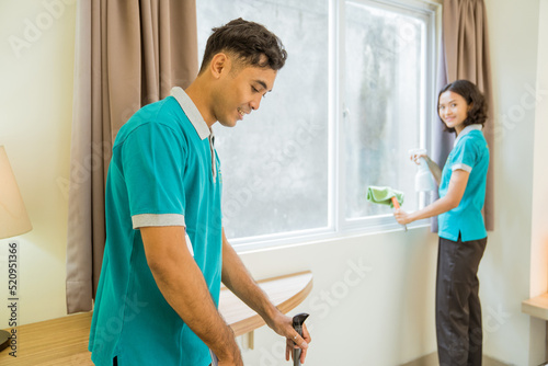 two housekeeper in turquoise uniform cleaning window and floor in the hotel room