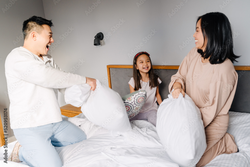 Asian family with little girl fighting with pillows together in bed Asian family with little girl fighting with pillows together in bed