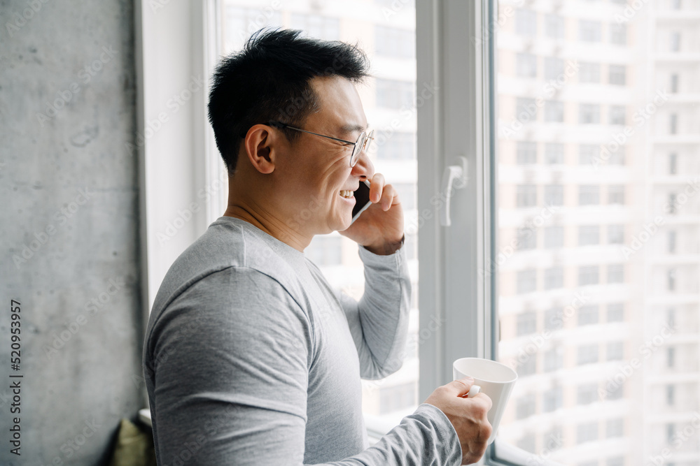 Asian man smiling and talking on mobile phone while drinking coffee Asian man smiling and talking on mobile phone while drinking coffee