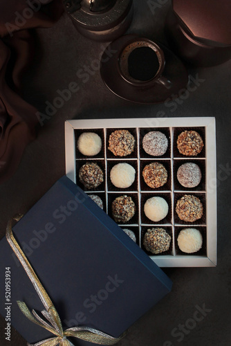 Handmade chocolates. Handmade candies in a square box with a blue lid. Festive packaging.Vertical photo on dark background.Flat lay.Top view.