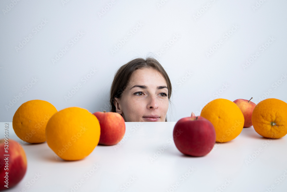 Young woman looks at fruits lying on a white table against a white wall