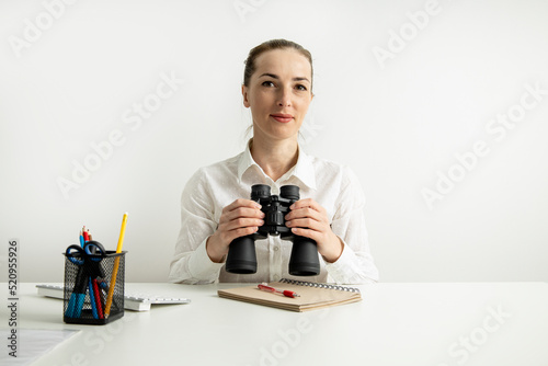 Young woman with binoculars sitting in the office at the workplace