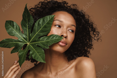 Black curly shirtless woman posing with green leaf
