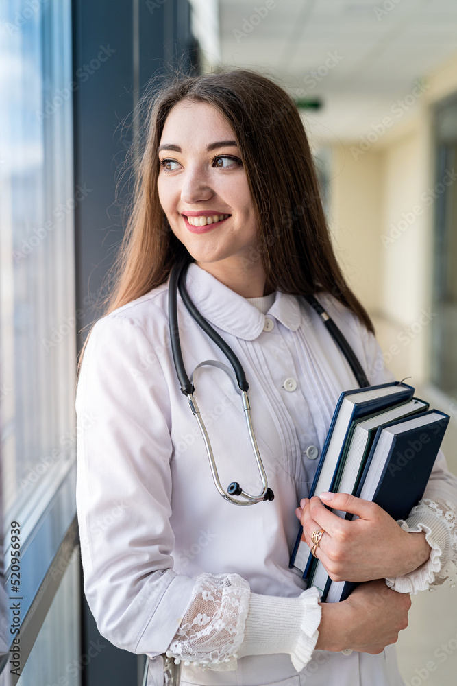 smiling young female doctor in uniform with stethoscope holding book while standing smiling young female doctor in uniform with stethoscope holding book while standing
