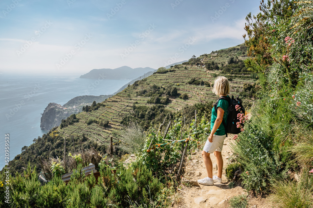 Active sporty girl hiking in Cinque Terre,Italy.View of coastline and sea.Woman backpacker on steep cliff enjoying freedom,adventure,summer holiday.Scenic Italian Riviera landscape.Travel background.