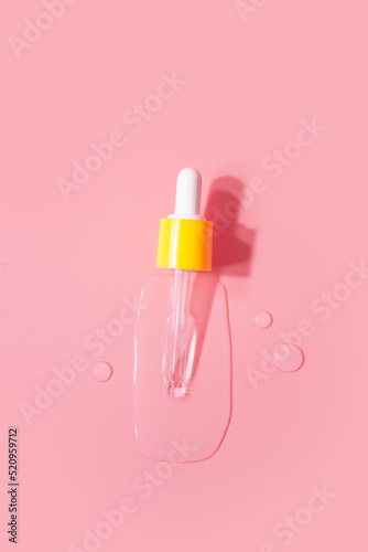 Yellow pipette drops of serum moisturized bottle on pink background. Essence transparent hyaluronic acid