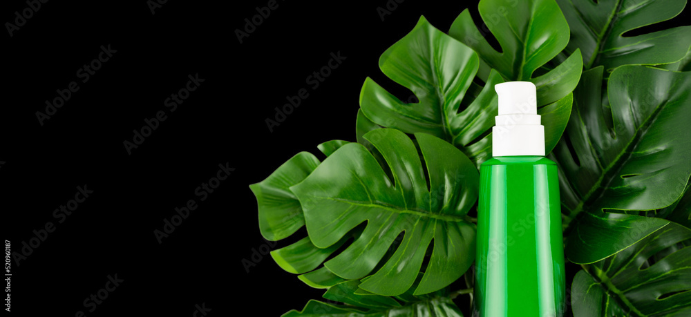 Opened green bottle with tropical monstera leaf on isolated black background close up. Brand packaging mockup. Aromatic oil, skin care beauty product, cream or serum. Natural herbal cosmetics concept Opened green bottle with tropical monstera leaf on isolated black background close up. Brand packaging mockup. Aromatic oil, skin care beauty product, cream or serum. Natural herbal cosmetics concept