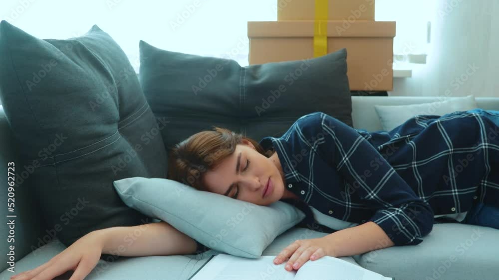 Beautiful young Caucasian woman lying on sofa in living room fallen asleep with book in new apartment with many boxes. Loving husband covers his wife with a blanket. Slow motion Beautiful young Caucasian woman lying on sofa in living room fallen asleep with book in new apartment with many boxes. Loving husband covers his wife with a blanket. Slow motion