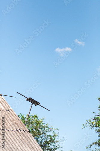 An old antenna on the roof against a blue clean sky with parts of the trees on the background