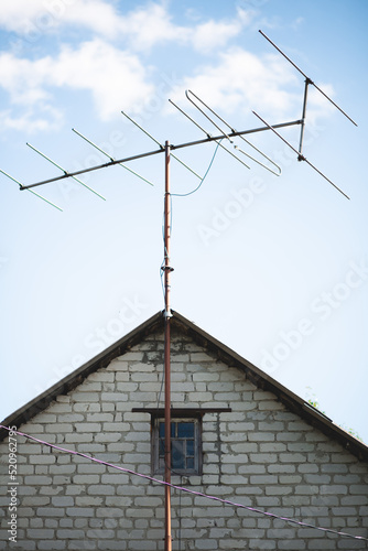 An old antenna on the roof against a blue c;oudy sky. A small old window is on the center of the frame
