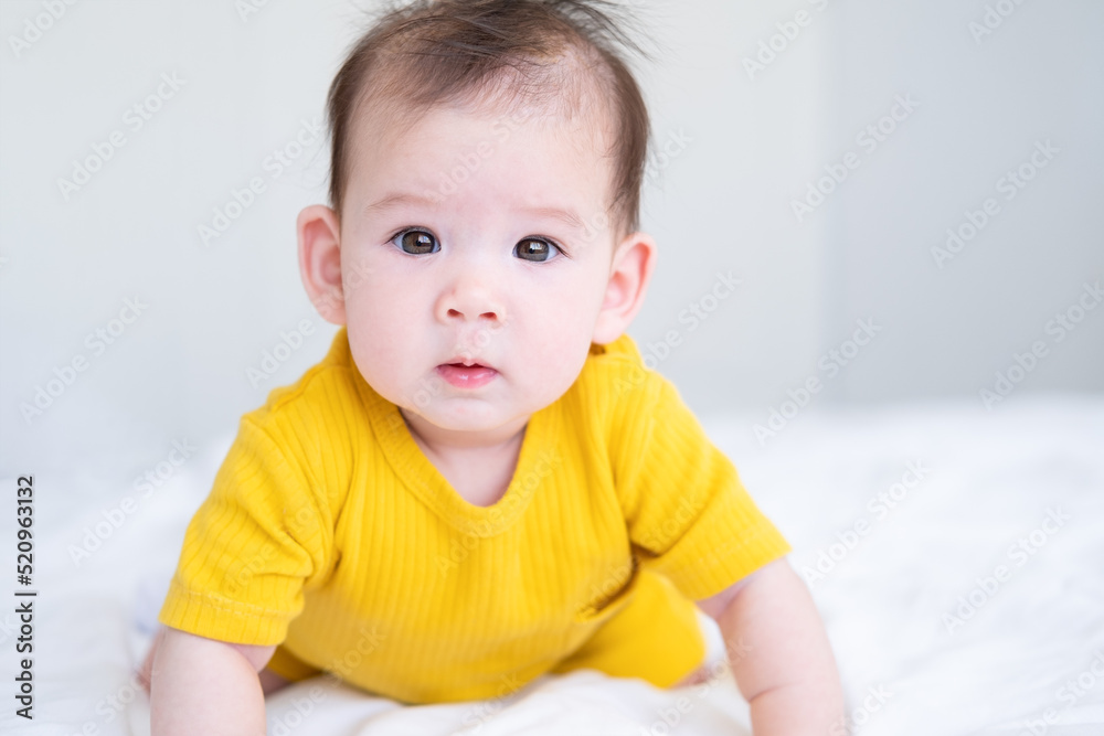 healthy asian baby girl 5 months in yellow bodysuit on bed on white bedding healthy asian baby girl 5 months in yellow bodysuit on bed on white bedding