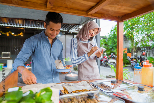 muslim couple ordering food to break fasting in traditional food market stall served by the seller
