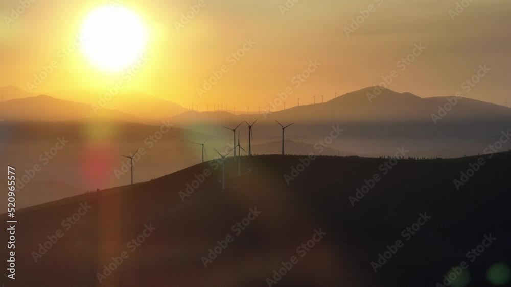 Multiple wind turbines at sunrise standing on a hill. Multiple wind turbines at sunrise standing on a hill.