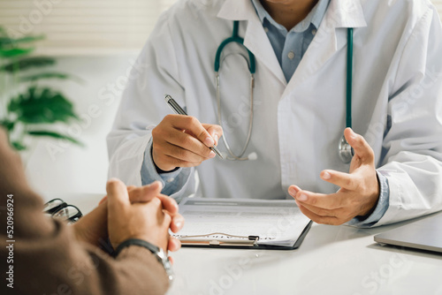 Fototapet A professional physician in a white medical uniform talks to discuss results or symptoms and gives a recommendation to a male patient and signs a medical paper at an appointment visit in the clinic