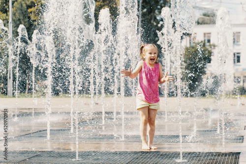 little girl playing with small fountains in the town square on a hot summer day