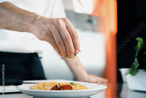 Close-up of a chef sprinkling French omelet with finely chopped herbs in a professional kitchen