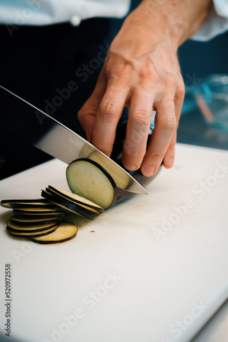 Close-up of a chef slicing eggplant in a professional restaurant kitchen