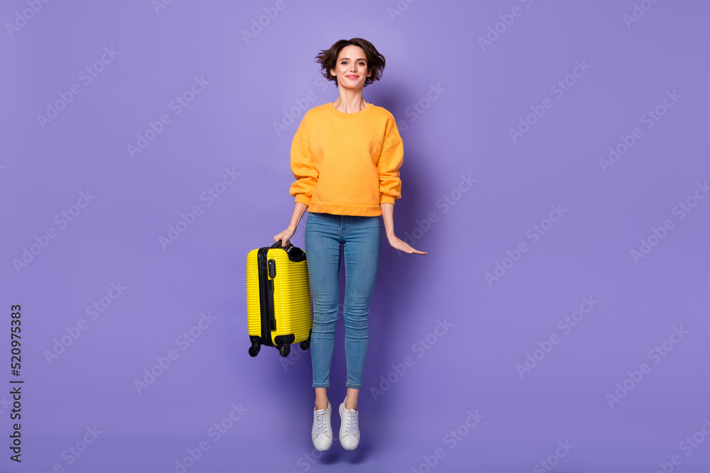 Full length body size view of attractive cheerful girl jumping holding suit case isolated over violet lilac color background Full length body size view of attractive cheerful girl jumping holding suit case isolated over violet lilac color background