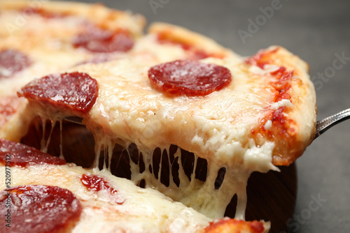Taking slice of tasty pepperoni pizza on table, closeup