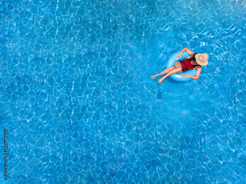 Zenith aerial view of a swimming pool in summer. Young girl in a swimsuit and hat floating with blue donut.