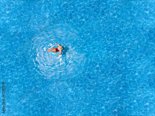 Zenith aerial view of a swimming pool in summer. Young girl in a swimsuit and hat floating with blue donut.