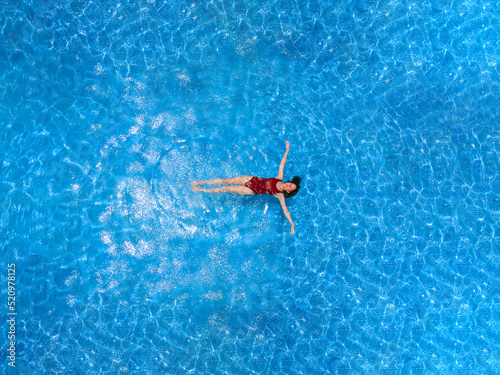 Aerial view of a swimming pool in summer. Young woman in a swimsuit swimming and refreshing.