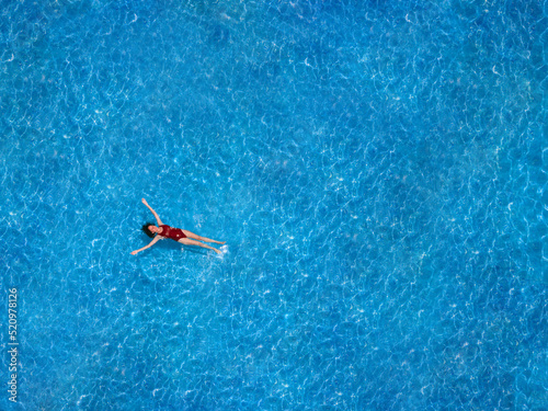 Aerial view of a swimming pool in summer. Young woman in a swimsuit swimming and refreshing.