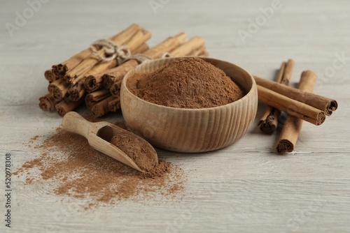 Aromatic cinnamon powder and sticks on white wooden table photo