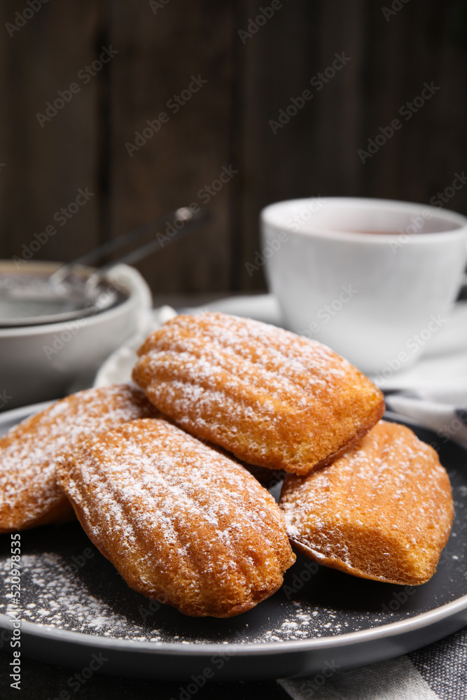 Delicious madeleine cakes with powdered sugar on table, closeup