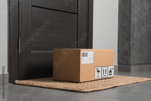Cardboard box on floor mat near entrance. Parcel delivery service