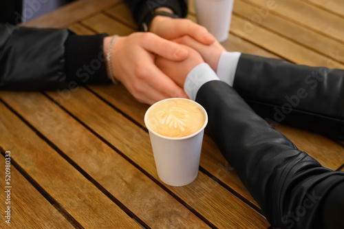 Lovely couple with coffee holding hands together at wooden table  closeup. Romantic date