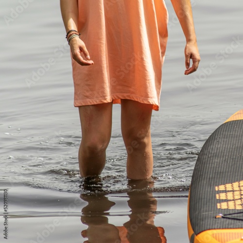 mulher a caminhar na água do lago junto a prancha de stand up paddle