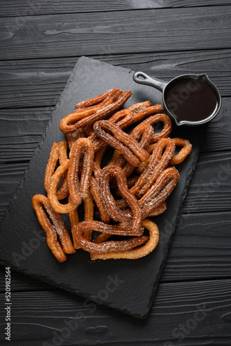 Homemade churros with chocolate on a dark wooden rustic background.