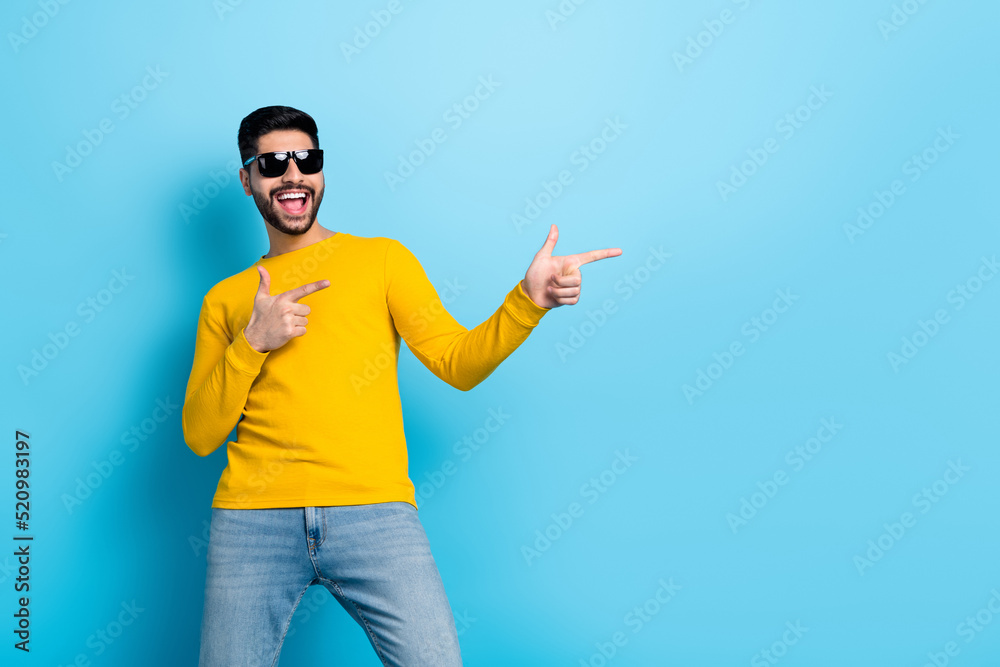 Naklejka premium Photo of pretty excited man wear yellow sweater dark glasses dancing pointing empty space isolated blue color background