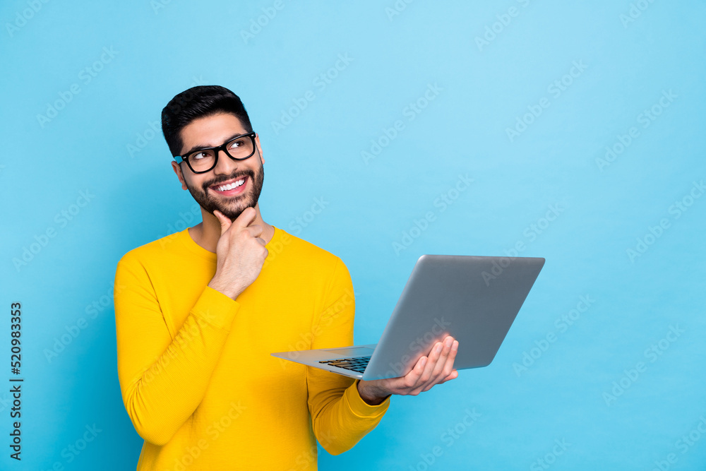 Photo of creative minded man hand touch chin look empty space hold netbook isolated on blue color background Photo of creative minded man hand touch chin look empty space hold netbook isolated on blue color background